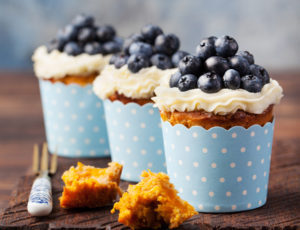 Pumpkin cupcakes decorated with cream cheese frosting and fresh blueberries on a wooden background Copy space