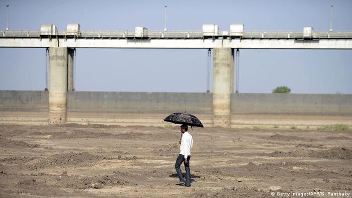 An Indian man holds an umbrella as he walks on the dry reservoir bed next to Gunda Dam in India